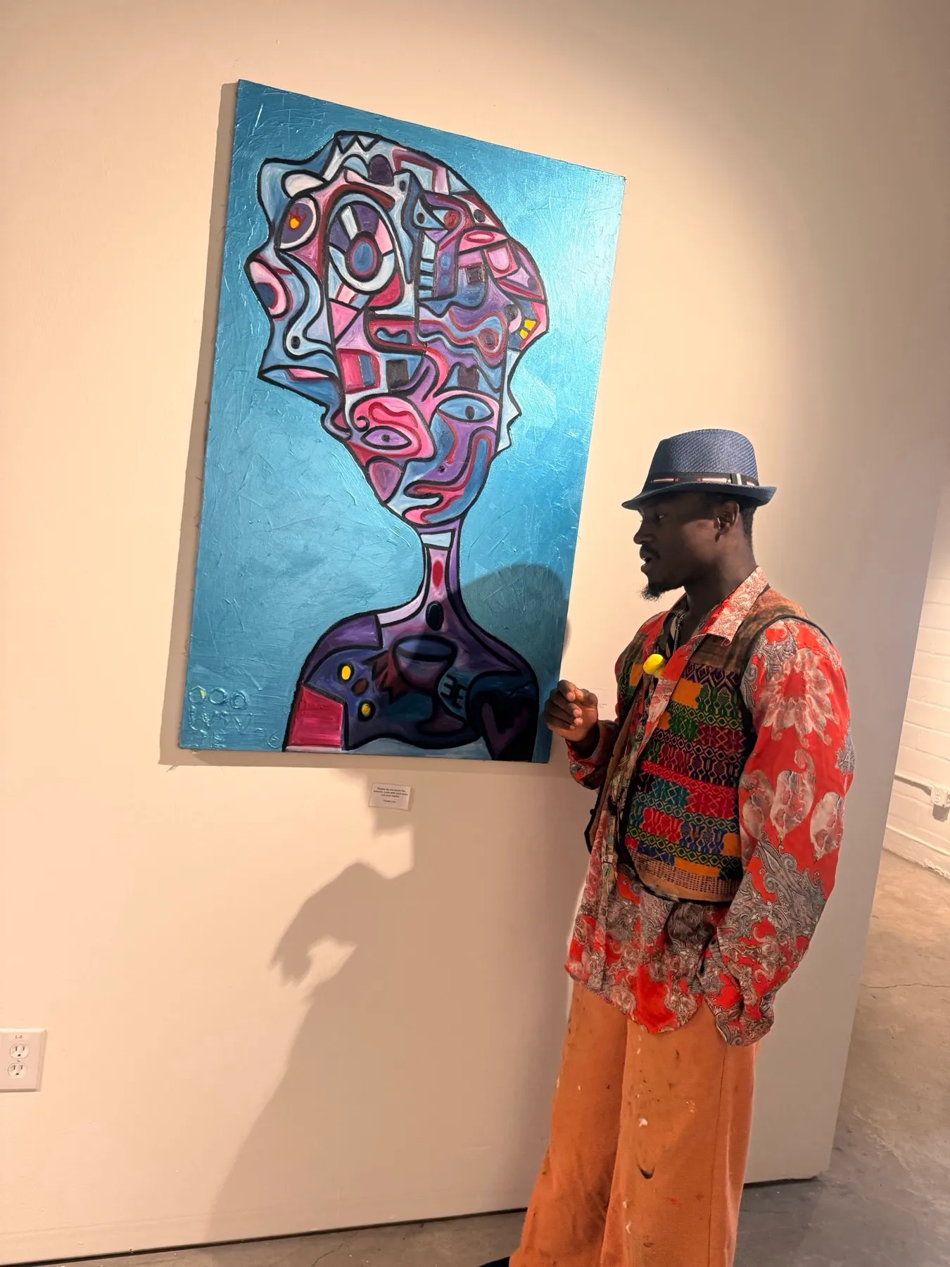 Ooowwee Walker presenting his metallic-blue profile portrait canvas in a gallery