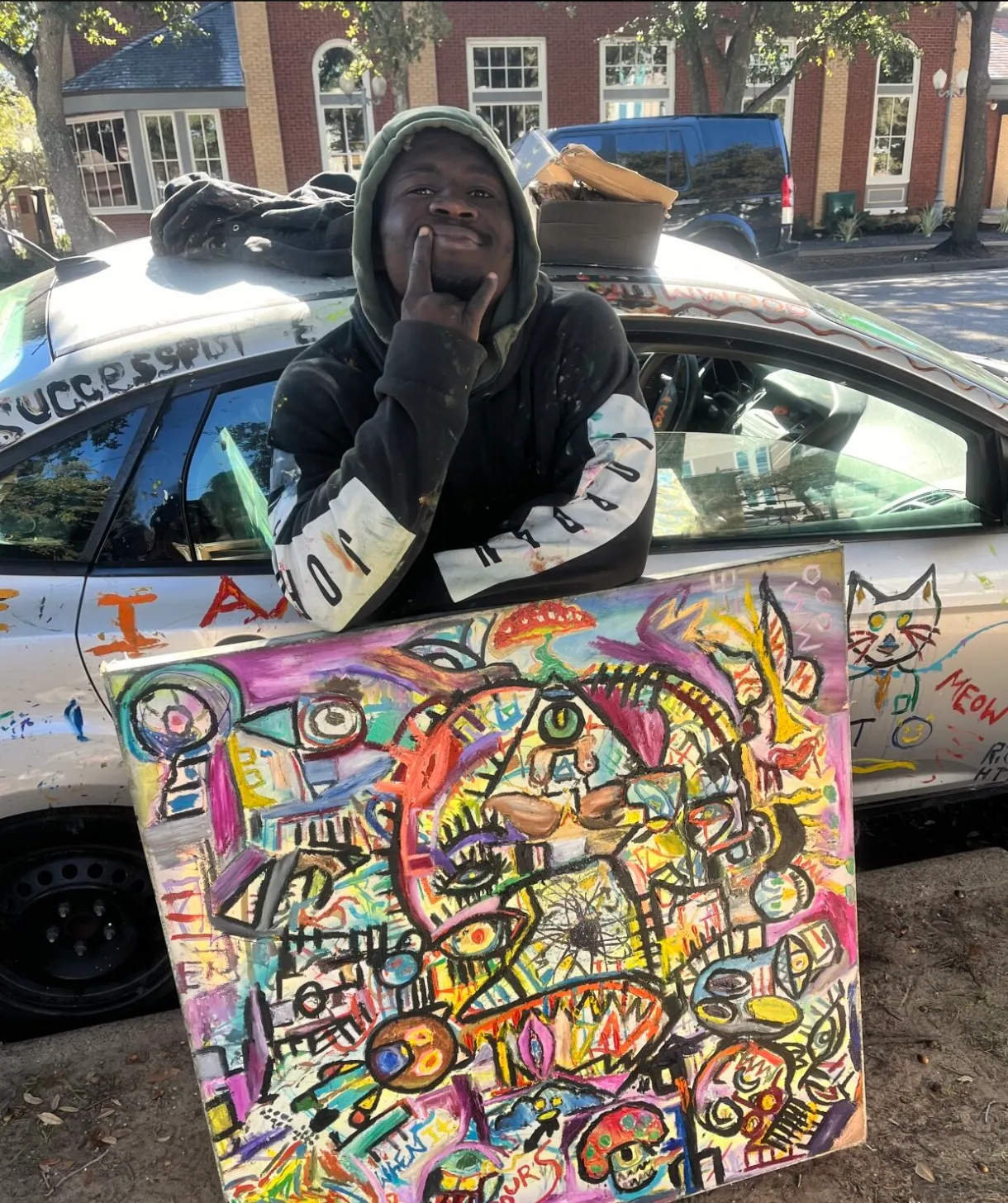 Ooowwee grinning out the window of his hand-painted car, holding a canvas -- SUCCESSFUL painted up top, a MEOW cat on the back door