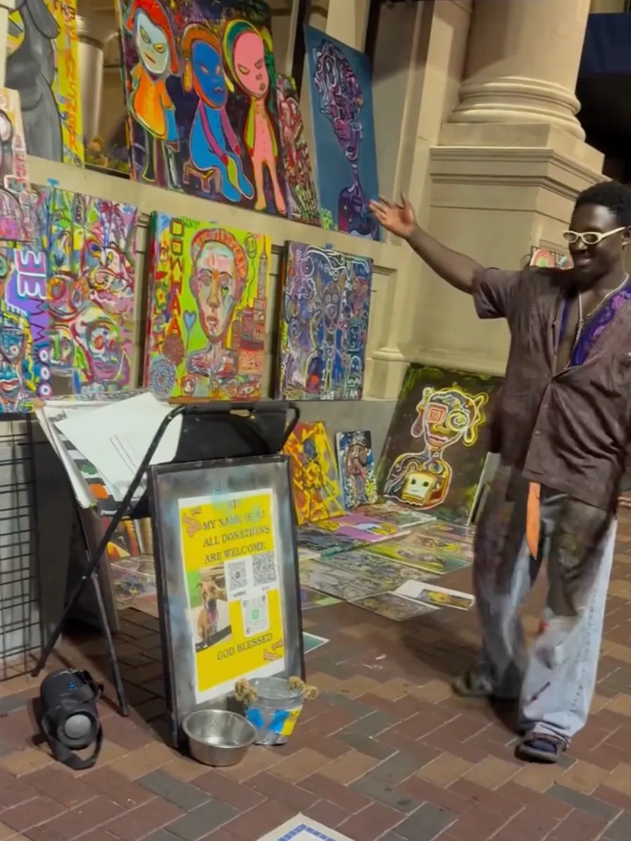 Ooowwee presenting his wall of paintings on the street at night, arm out like a game-show host