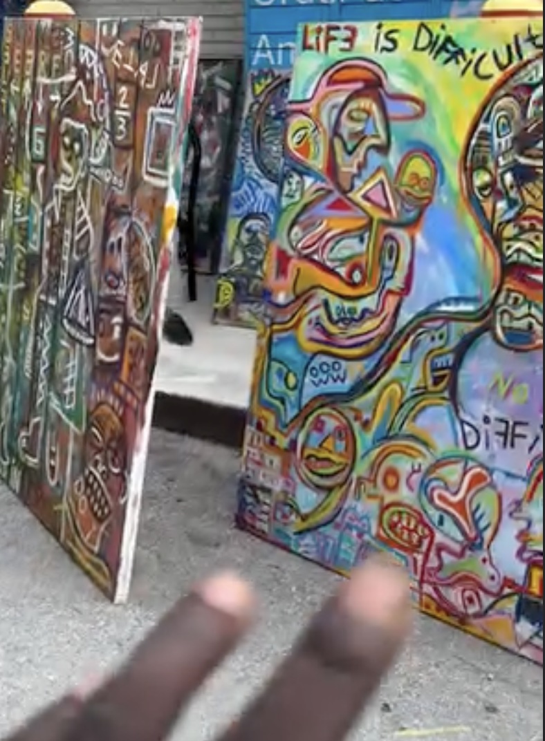 Street display of canvases including one that reads LIFE IS DIFFICULT, painted over with NO DIFFICULTY
