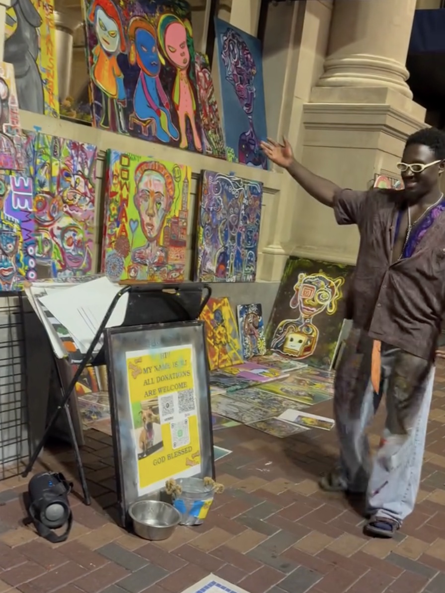 Ooowwee presenting his wall of paintings on the street at night, arm out like a game-show host